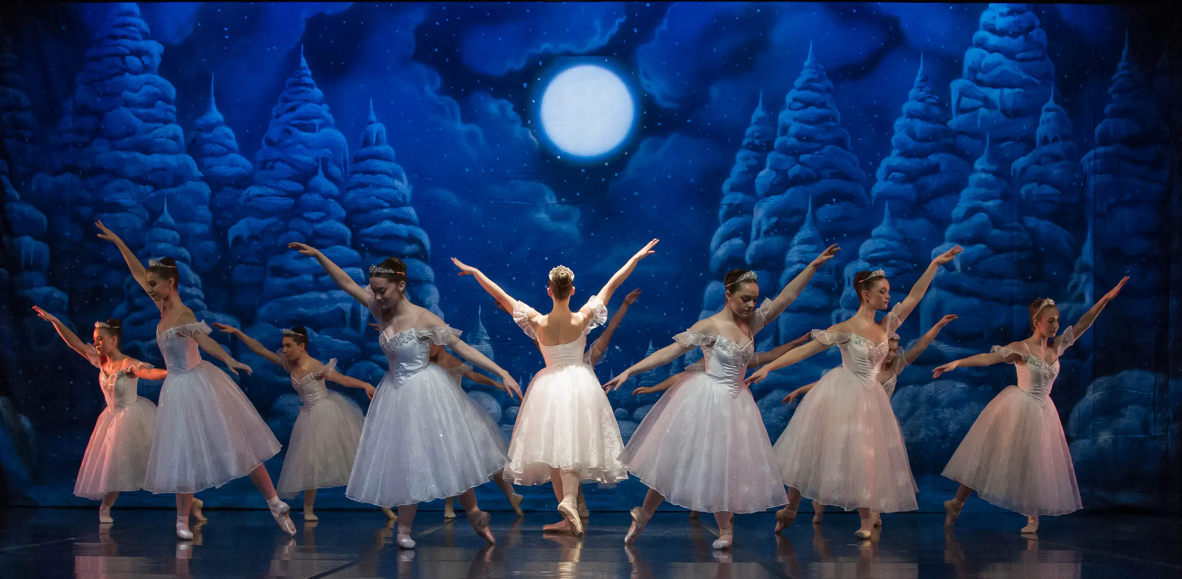 Ballet for Youth snowflake dancers on stage beneath a full moon in the Nutcracker’s snow scene